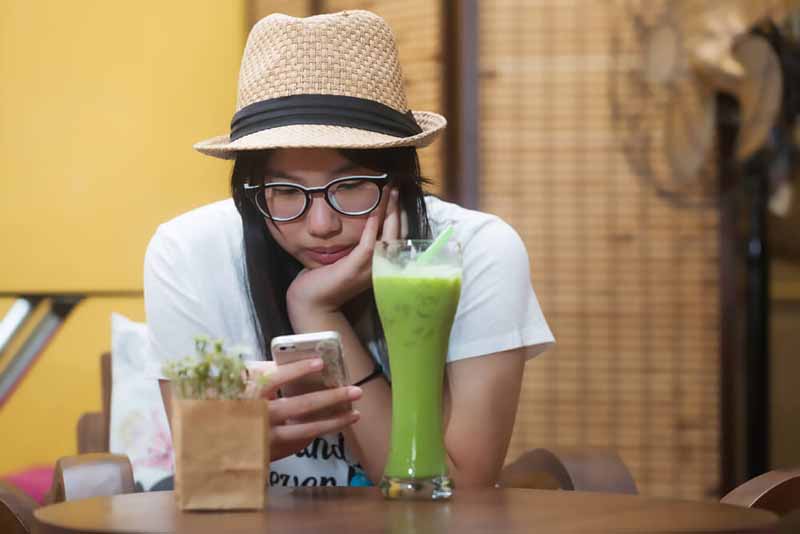 Dievča v klobúku sleduje jej telefón v kaviarni.